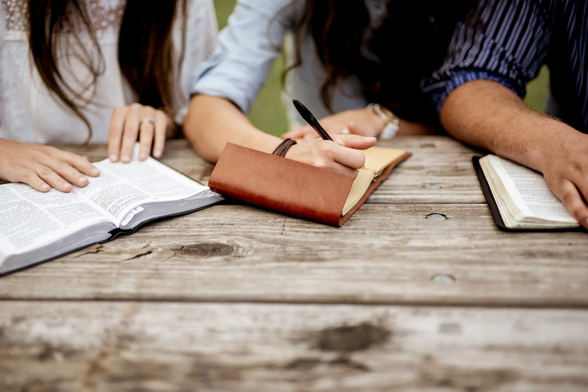 Closeup shot of people sitting near each other and reading the bible